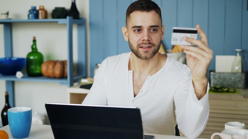 A person holding a credit card while looking at a laptop
