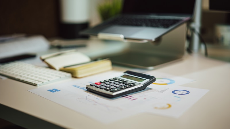 A calculator and laptop on a home-office desk with financial documents