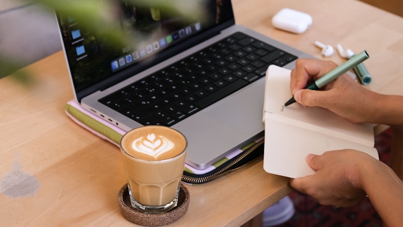 A founder writing notes in a notebook next to a laptop